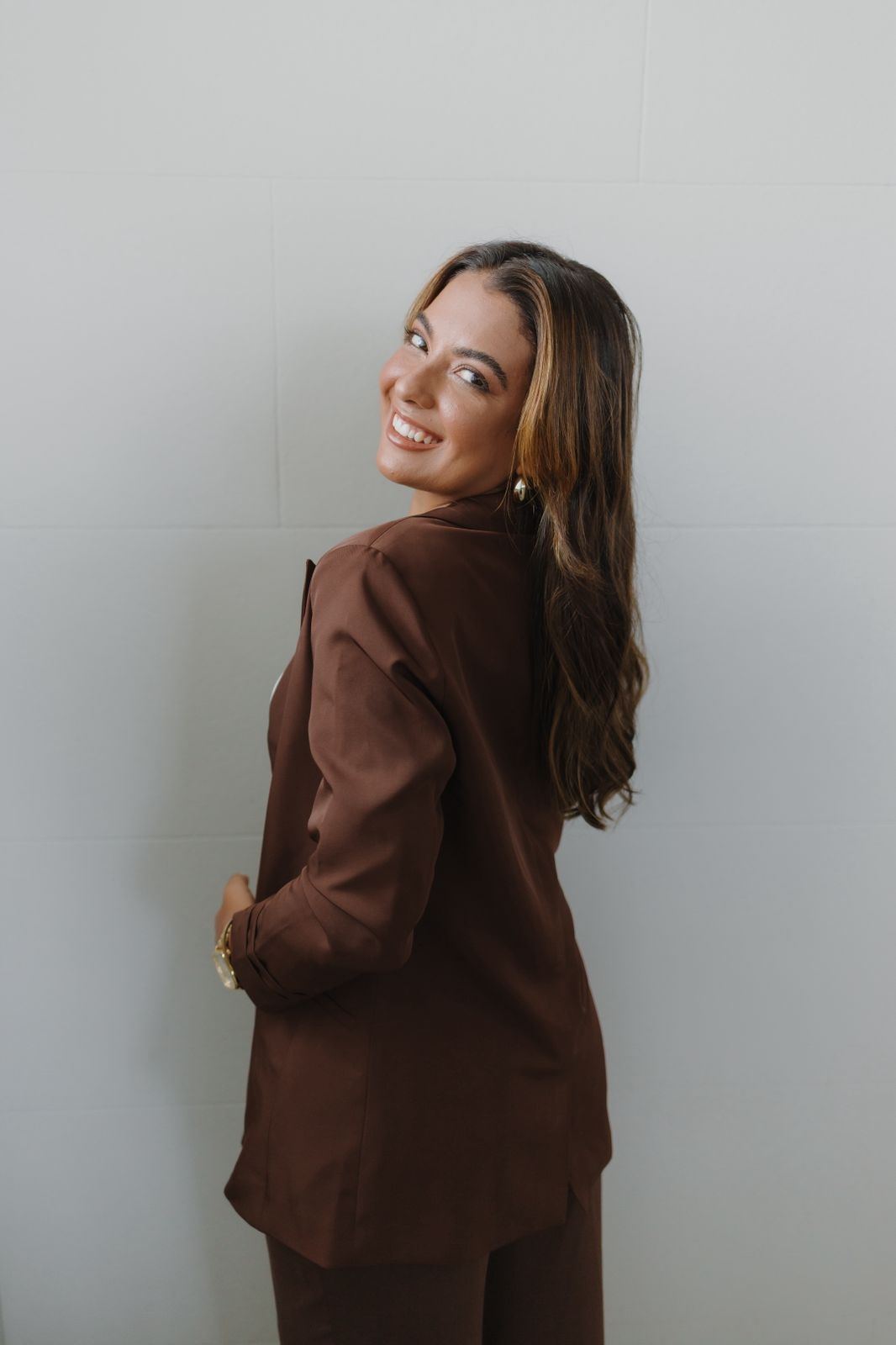 Amanda Prado em blazer marrom olhando por cima do ombro
